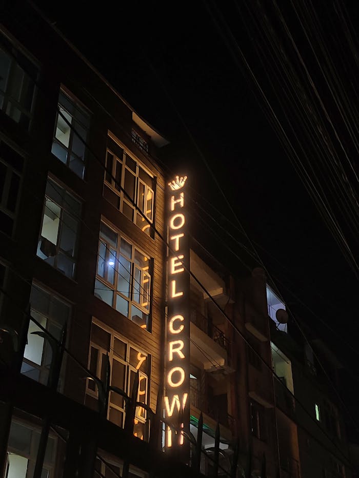 A neon-lit Hotel Crow sign shines brightly at night against an urban building facade.